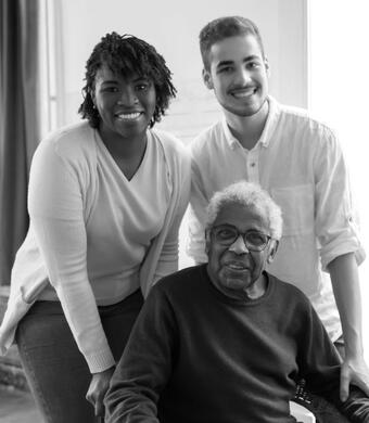 Elder man is sitting at he table. Middle age woman and a child are standing behind him. Elder man is sitting at he table. Middle age woman and a child are standing behind him.